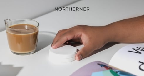 Dose mit Snus liegt auf einem Tisch und eine Hand hebt sie auf
