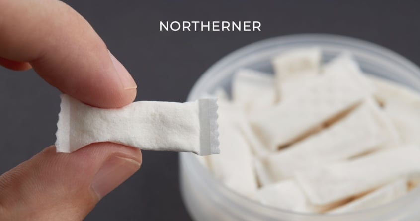 Ein Snus wird vor eine offene Dose mit Snus gehalten