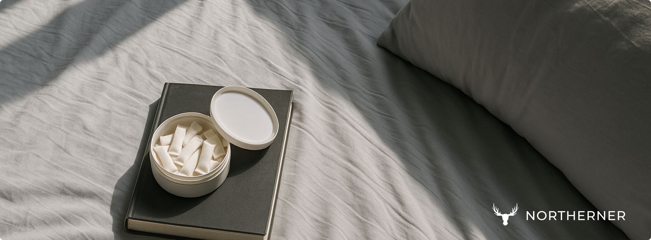 nicotine pouches in a can lie on top of a book, on a bed